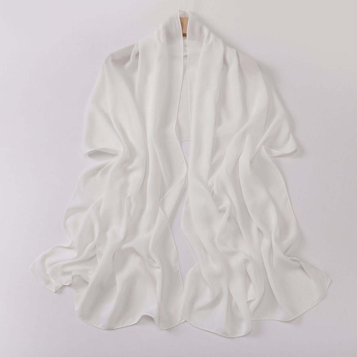 White scarf draped over a wooden stick on a light gray background